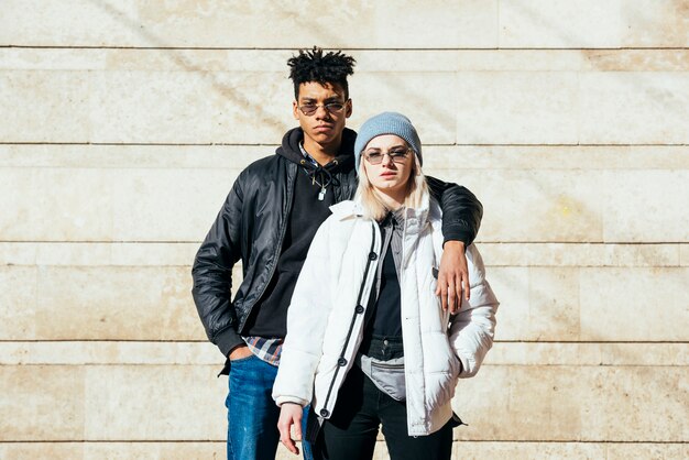 Portrait of young couple in fashionable clothes standing against wall