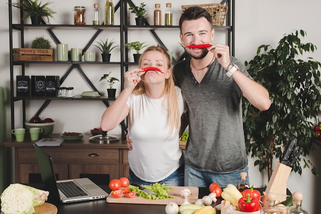 キッチンの鼻の上に赤い唐辛子を持つ若いカップルの肖像