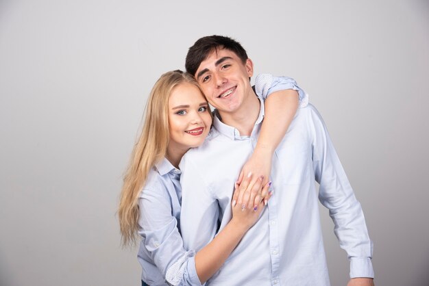 Portrait of young couple hugging each other over gray wall.