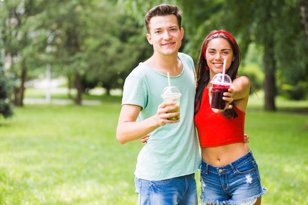 Portrait of young couple offering healthy smoothies in the park