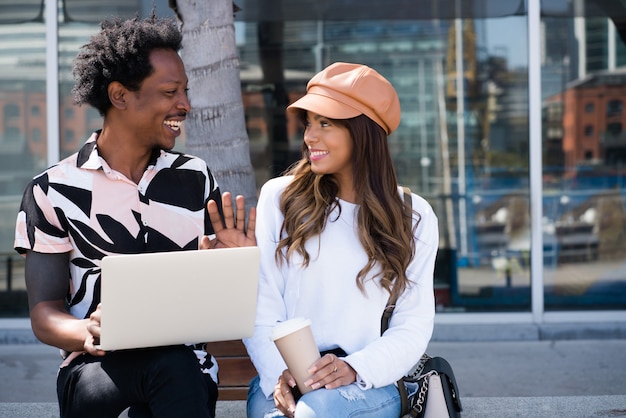 Portrait of young couple using laptop while sitting outdoors on the street