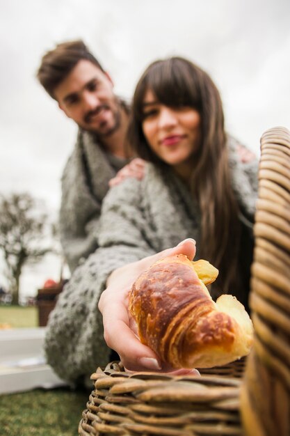 Portrait of young couple wrapped in gray blanket giving baked croissants