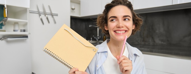 Free photo portrait of young creative woman holding her notebook and smiling makes notes in her diary writing