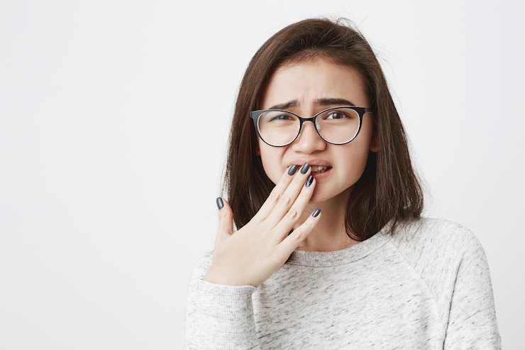 無料Photo メガネの若いかわいい女性の肖像画、目を細めて、手で口を覆っている、痛みを感じている、または申し訳ありません