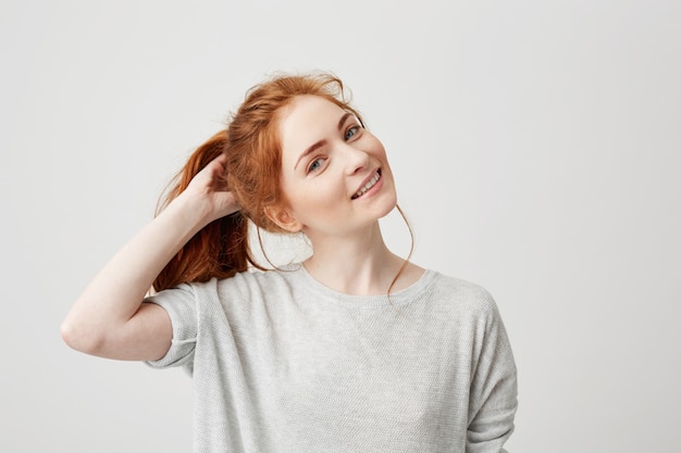 Portrait of young cute redhead girl smiling touching hair .