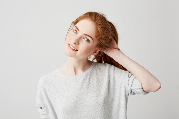 Portrait of young cute redhead girl smiling touching hair .