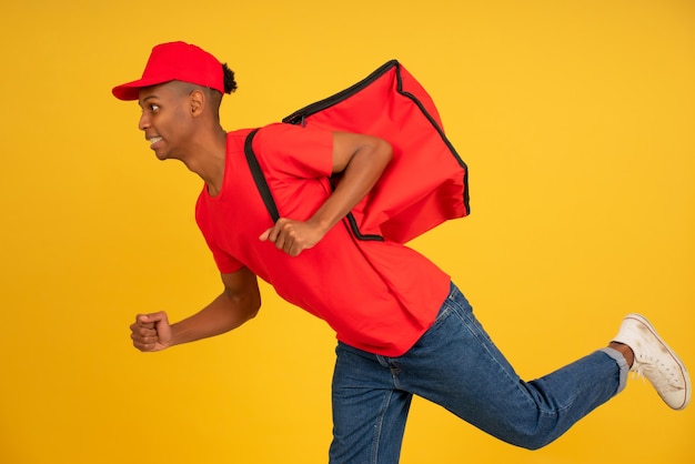 孤立した背景の上を走っている赤い制服を着た若い配達人の肖像画。配信のコンセプト。