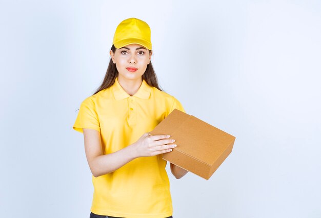 Portrait of young deliverywoman holding single box on white.