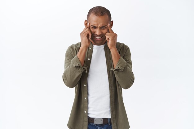 Portrait of young depressed or sick africanamerican man feeling severe headache suffer migraine touching temples grimacing from pain cant stand painful symptom white background
