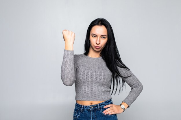 Portrait of young dominating brunette woman showing fist on gray wall