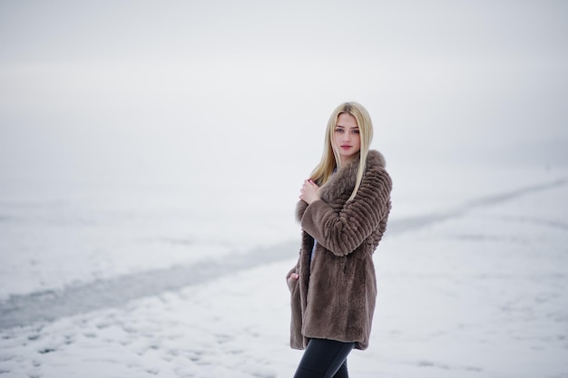 Ritratto di giovane eleganza ragazza bionda in una pelliccia di sfondo fiume nebbioso sul ghiaccio d'inverno