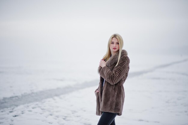 Portrait of young elegance blonde girl in a fur coat background foggy river on winter ice