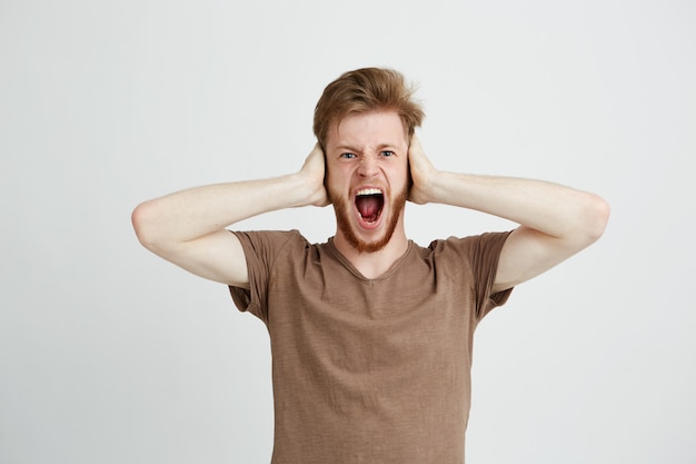 Portrait of young emotive angry man closing ears shouting screaming.