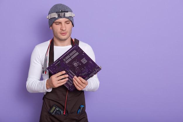 Portrait of young experienced radiotrician standing isolated over lilac in studio, holding electronic circuit board