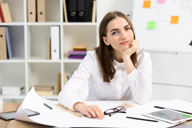 Portrait of a young female architect sitting at desk looking to camera