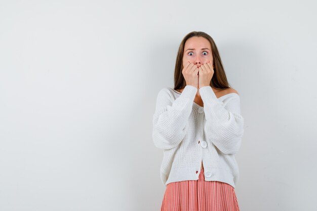 Portrait of young female biting fists emotionally in cardigan isolated