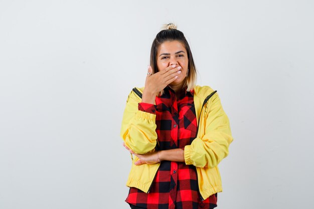 Foto gratuita ritratto di giovane donna che copre la bocca con la mano in camicia a scacchi, giacca e guardando stanco vista frontale