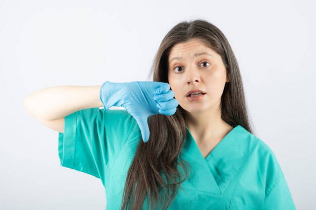 Portrait of a young female doctor in green uniform showing a thumb down .