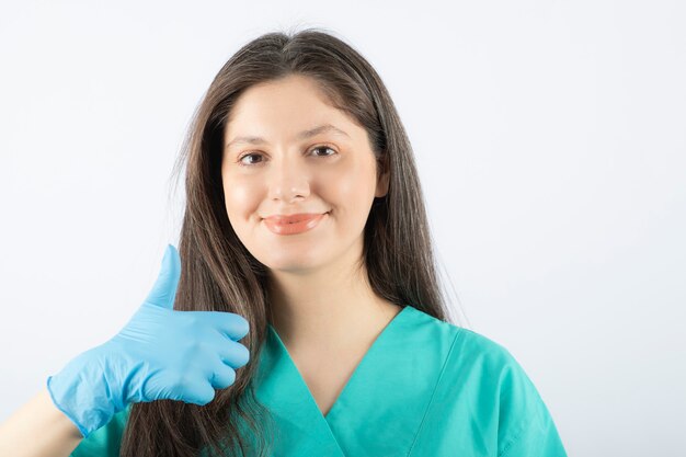 Portrait of a young female doctor in green uniform showing a thumb up. 