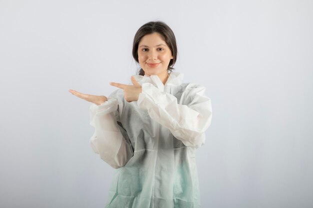Portrait of young female doctor scientist in defensive lab coat pointing away. 