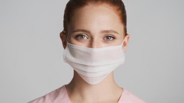 Портрет молодой женщины-врача в медицинской маске, счастливо смотрящей в камеру на белом фоне Концепция безопасности