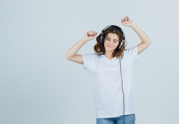 흰색 티셔츠, 청바지에 헤드폰으로 음악을 즐기고 즐거운 전면보기를 찾고 젊은 여성의 초상화
