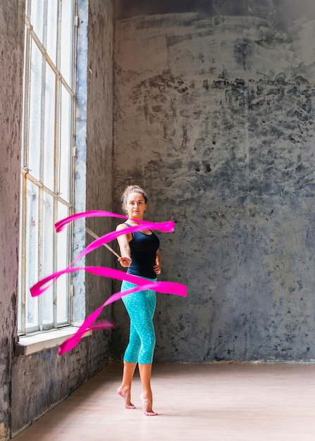 Foto gratuita ritratto di un ballerino giovane ginnasta femminile ballando con nastro rosa