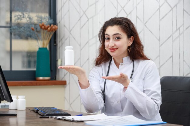 Портрет молодой работницы здравоохранения, держащей капсулу с лекарством и указывающей на нее рукой