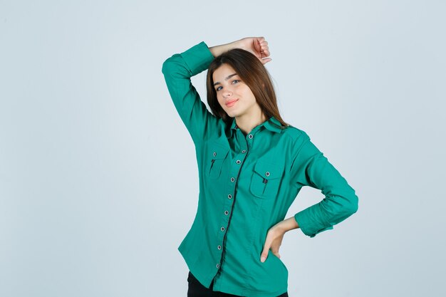 Портрет молодой женщины, держащей руку на голове в зеленой рубашке и выглядящей веселой, вид спереди