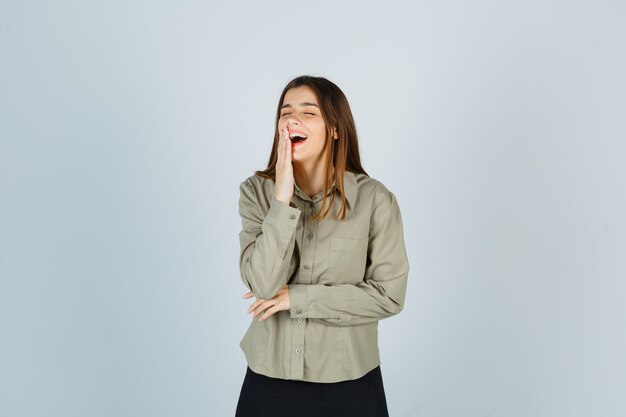 Portrait of young female keeping hand on mouth while laughing in shirt