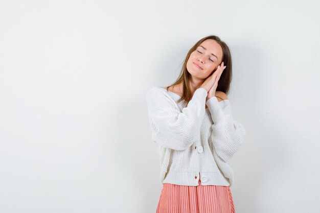 Portrait of young female leaning on palms as pillow in cardigan isolated