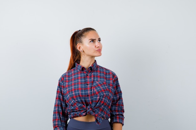 Портрет молодой женщины, глядя в клетчатую рубашку, брюки и задумчивый вид спереди