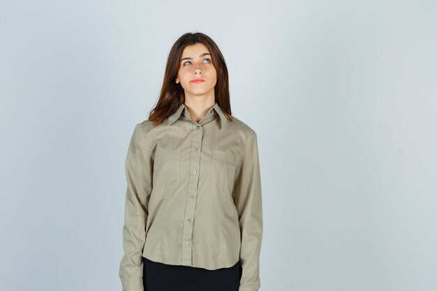 Portrait of young female looking up while curving lips in shirt