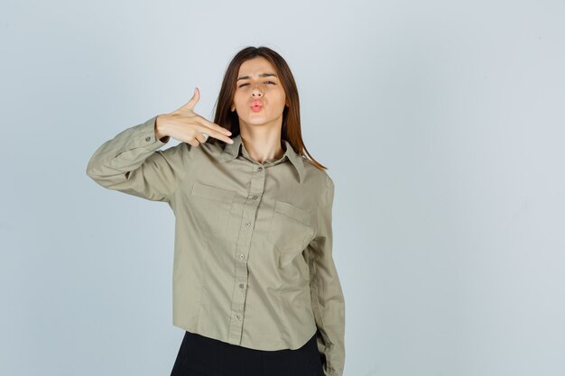 Портрет молодой женщины, делающей знак пальчикового пистолета, надувая губы в рубашке, юбке и уверенно выглядящей, вид спереди