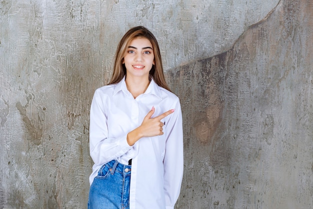 Free photo portrait of young female model standing and pointing over marble