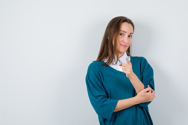 Портрет молодой женщины, указывающей вперед в свитере поверх рубашки и выглядящей разумным видом спереди