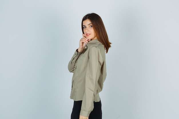 Portrait of young female posing while holding her chin with hand in shirt, skirt and looking confident