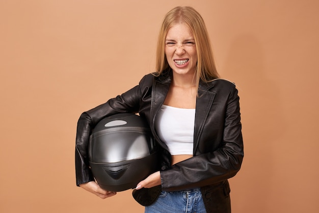 Portrait of young female rider with teeth braces and long straight hair posing isolated in black leather jacket