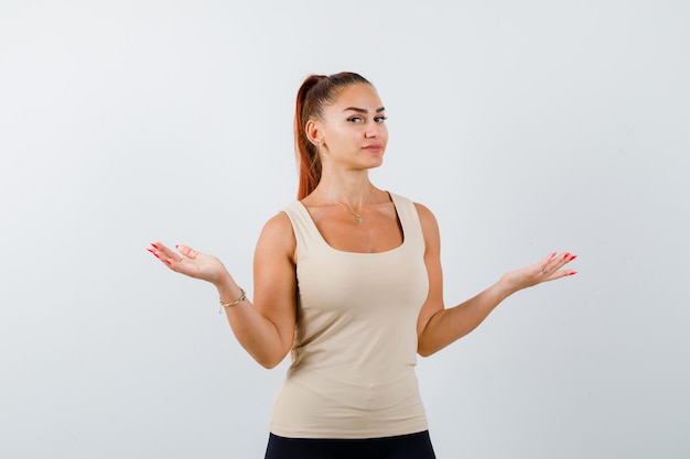 Free photo portrait of young female showing helpless gesture in beige tank top and looking clueless front view