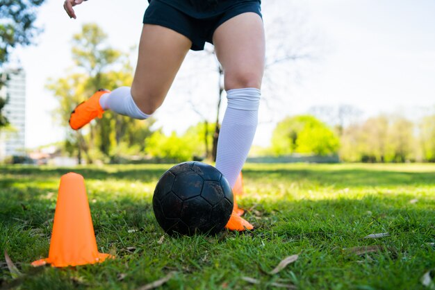 Портрет молодого женского футболиста бежать вокруг конусов пока практикующ с шариком на поле. Спортивная концепция.