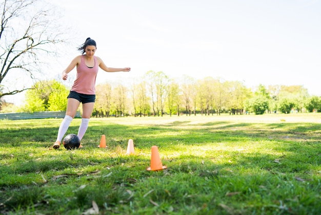 Portrait of young female soccer player running around cones while practicing with ball on field