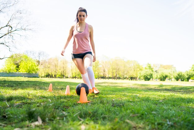 Portrait of young female soccer player running around cones while practicing with ball on field