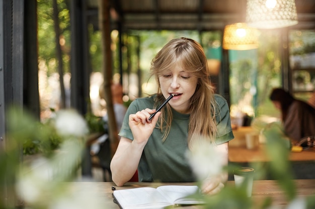 Портрет молодой студентки, жующей карандаш в кафе, готовясь к сдаче экзаменов