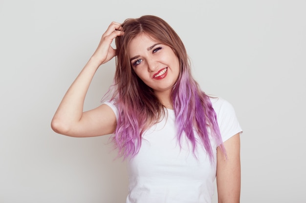 Portrait of young female in whiter casual style T-shirt scratching her hair from dandruff and irritation, suffering from lice, frowning face, isolated over grey background.