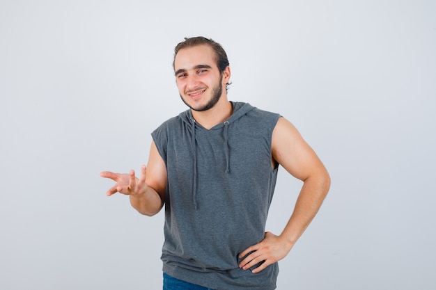 Портрет молодого здорового мужчины, протягивающего руку к камере в толстовке без рукавов и радостного вида спереди
