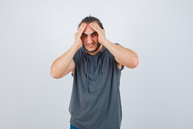 Portrait of young fit male suffering from headache in sleeveless hoodie  and looking painful front view