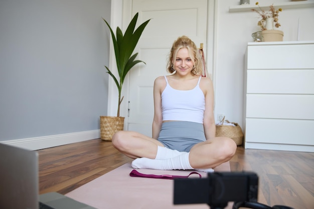 Free photo portrait of young fitness instructor vlogger showing exercises on camera recording herself sitting