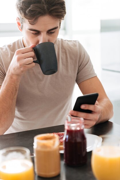 お茶を飲むと、スマートフォンを使用して焦点を当てた若者の肖像