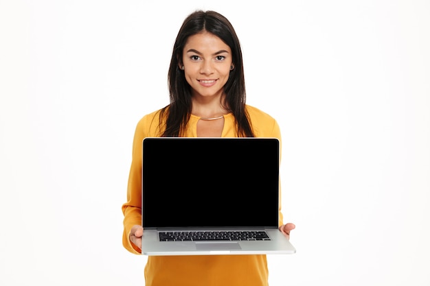 Портрет молодой дружелюбной женщины показывая портативный компьютер пустого экрана