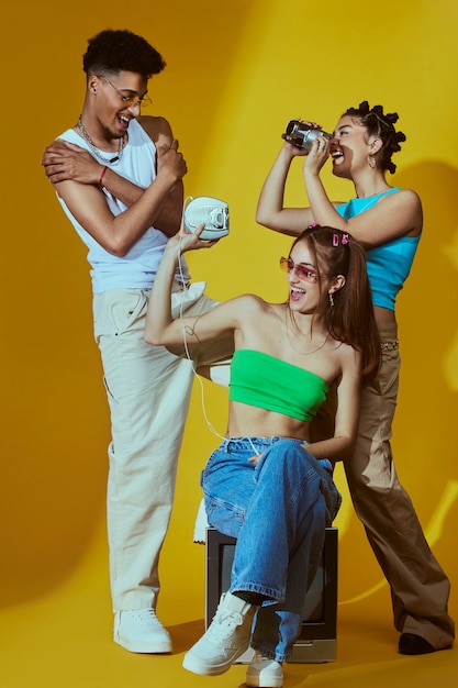 Портрет молодых друзей в стиле моды 2000-х, позирующих с портативным аудиоплеером и камерой